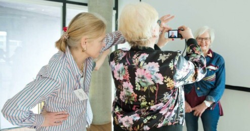 An older woman takes a photo of another older woman with her mobile phone. A cultural mediator gives tips.