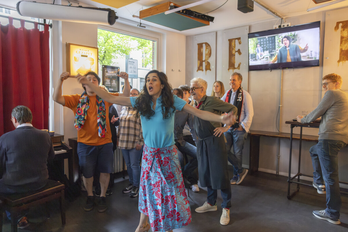 Eine Frau in einem langen geblümten Rock mit ausgebreiteten Armen und zum Singen geöffnetem Mund