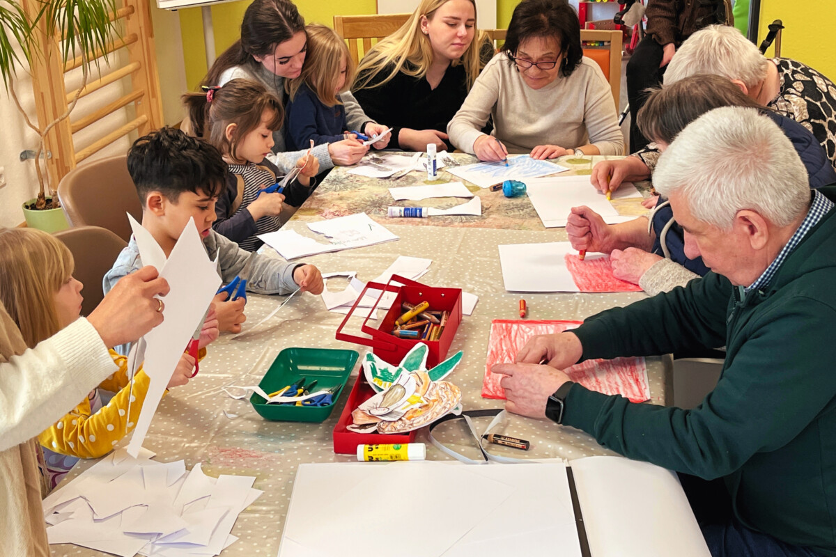 Eine Gruppe von alten Menschen und Kindern, die um einen Tisch sitzen und mit Papier basteln.