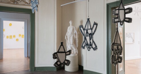 In einem mit Stuck verziehrten Ausstellungsraum hängen an Mobiles große, schwarz-weiß gemalte Tierfiguren. Im hintergrund ist eine antike Frauenstatue zu sehen.